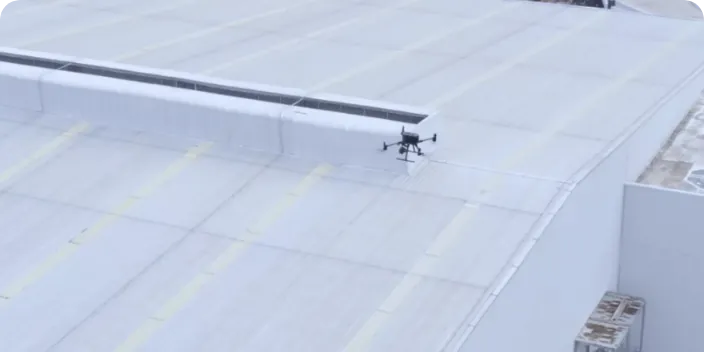 Black drone parked on a large white rooftop next to a parapet wall
